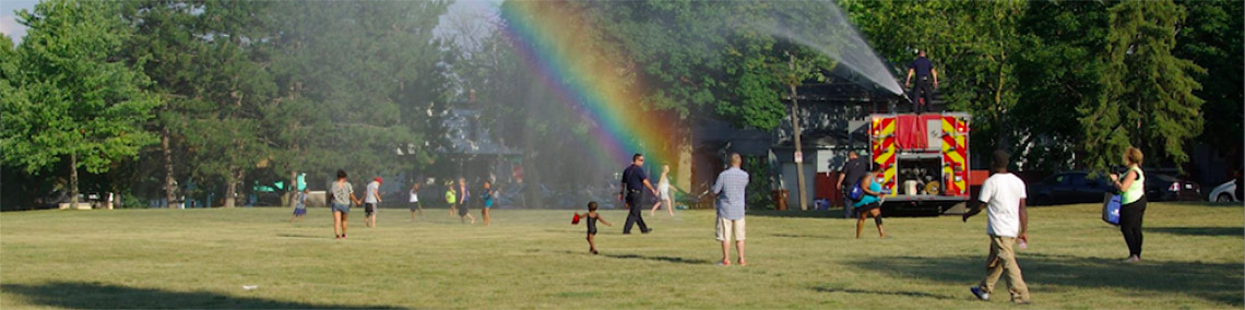 Photo of National Night out At Coit Park with a rainbow from a firetruck spraying water for the entertainment of children